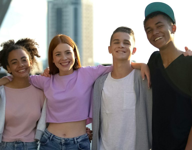 Four friends standing together with arms around each other, smiling
