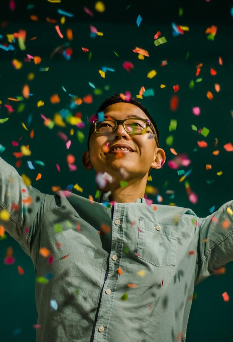 Young man celebrating joyfully as colourful confetti falls around him